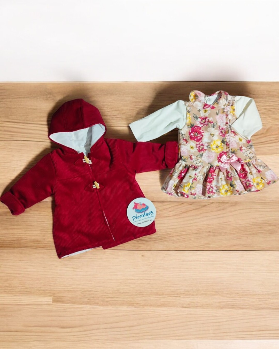 Conjunto infantil com casaco vermelho e vestido floral sobre madeira clara