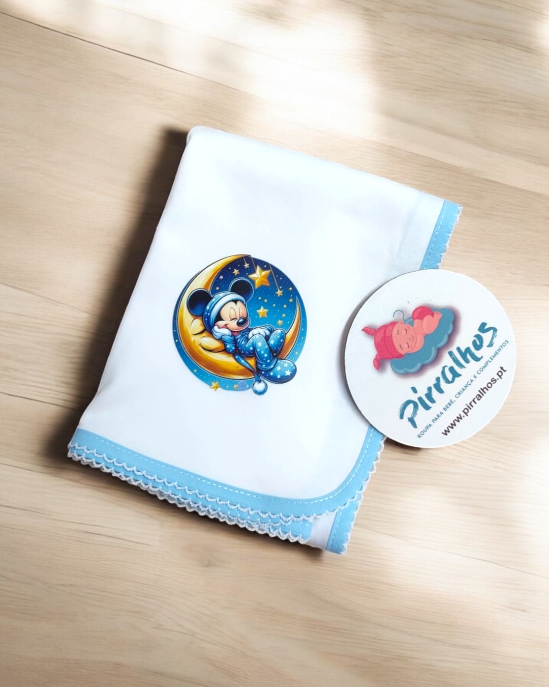 Toalha branca com borda azul e imagem de Mickey Mouse a dormir na lua e etiqueta Piralhos
