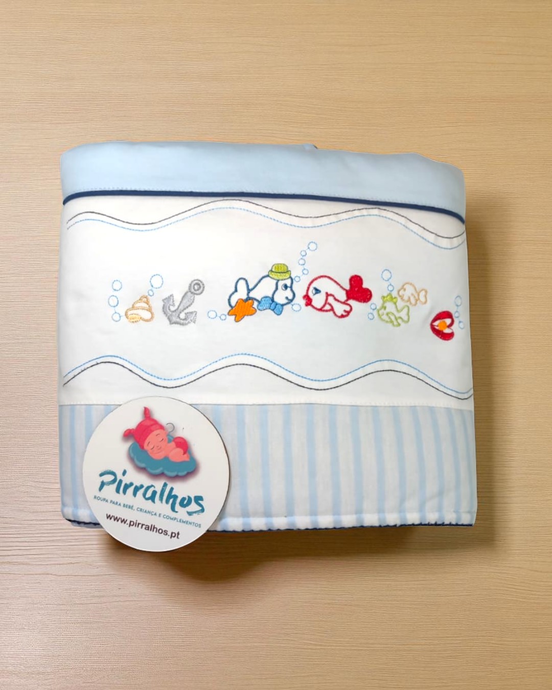 Manta azul e branca com peixes bordados e etiqueta da marca Pirralhos