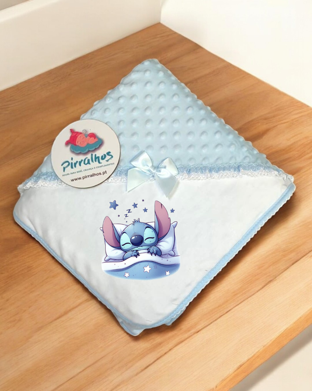 Manta de bebé azul com personagem Stitch a dormir, laço branco e renda, sobre madeira