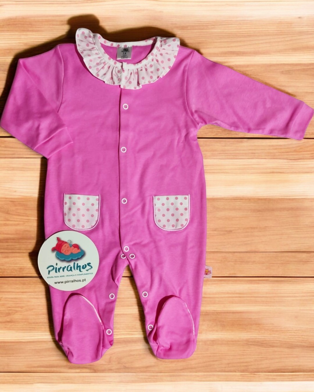 Macacão infantil rosa com gola e bolsos de bolinhas cor-de-rosa em branco sobre piso de madeira