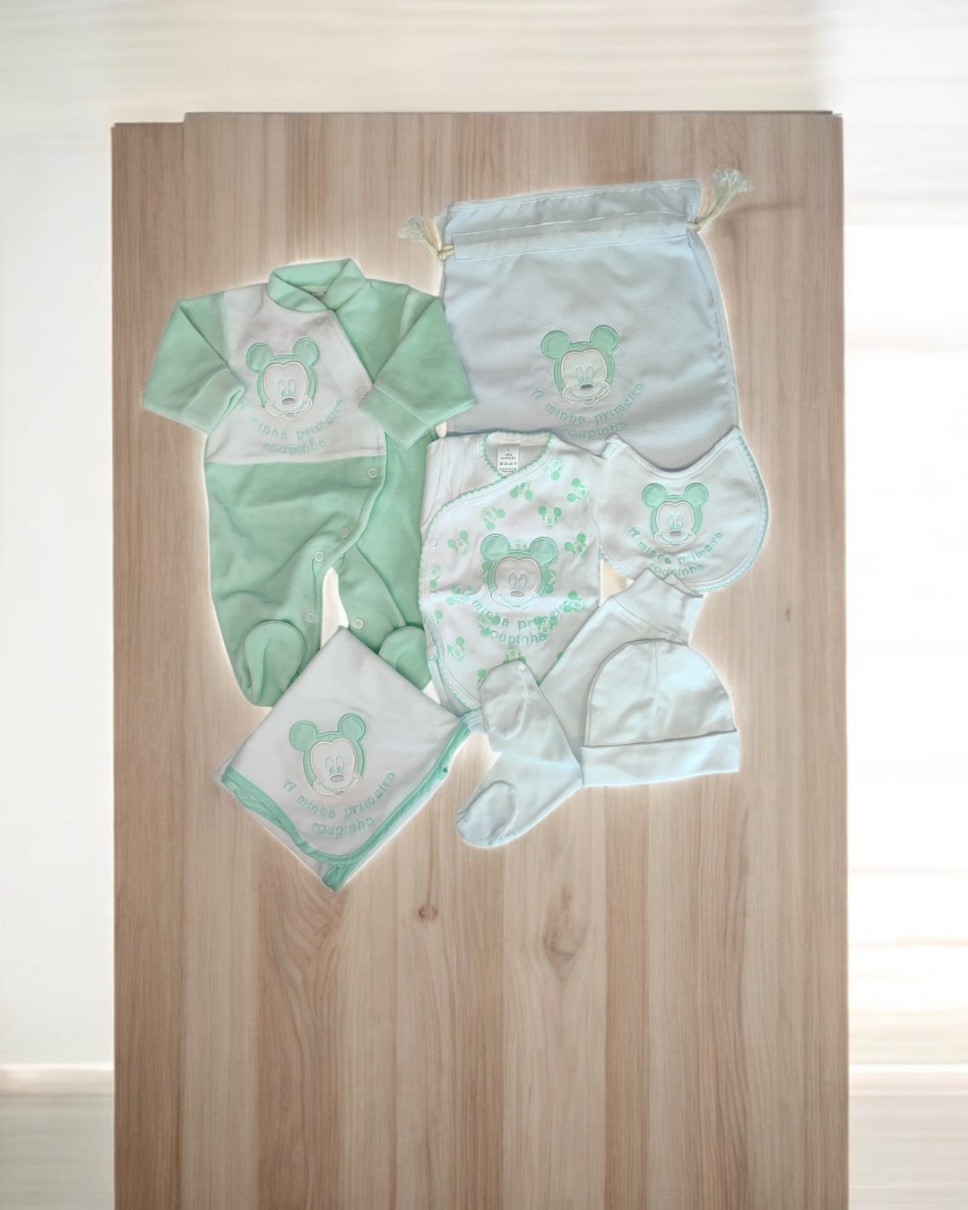 Conjunto de roupa para bebé verde e branco com urso e saco no fundo de madeira