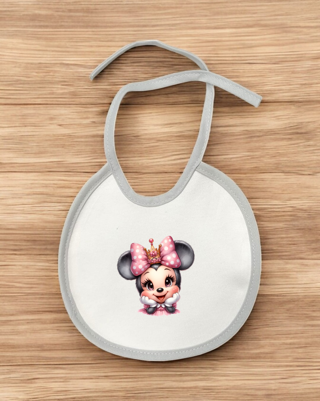 Babete branco com imagem de rato com laço rosa e coroa sobre madeira clara