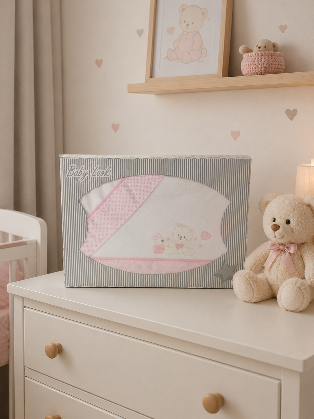 Manta de bebé branca e rosa em caixa Baby Look sobre cómoda branca com urso de peluche.
