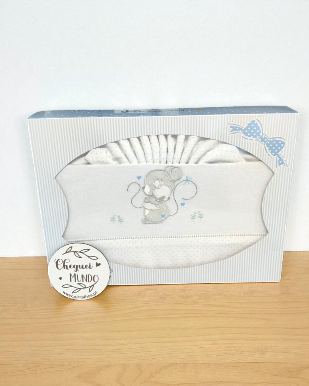 Conjunto de roupa de bebé branca com bordado de rato, em embalagem com riscas cinza e laço azul