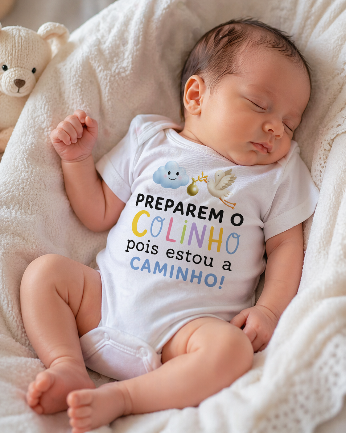 Bebé a dormir com body branco estampado colorido e ursinho de peluche ao lado