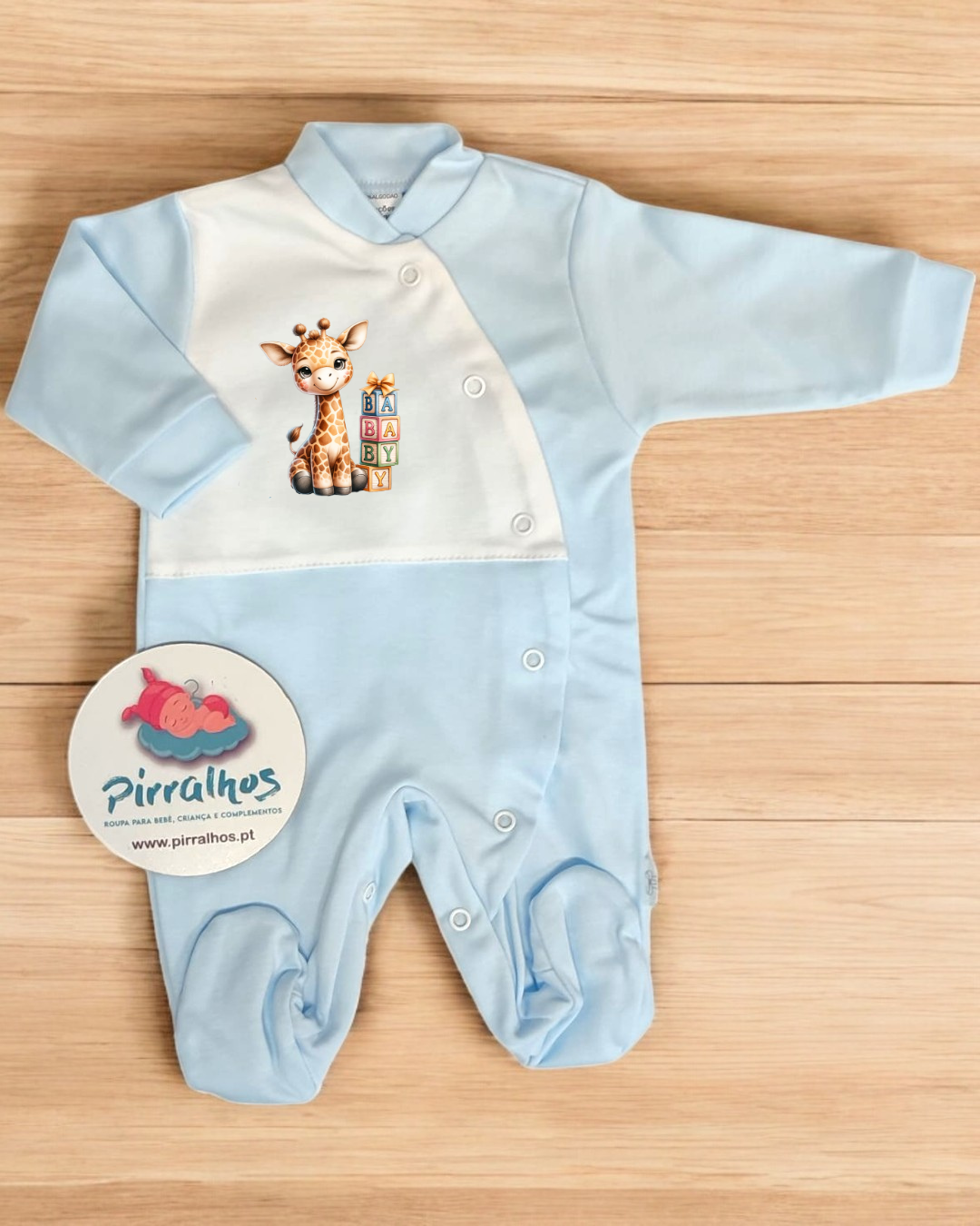 Macacão bebé azul claro e branco com girafa e cubos coloridos, sobre madeira clara