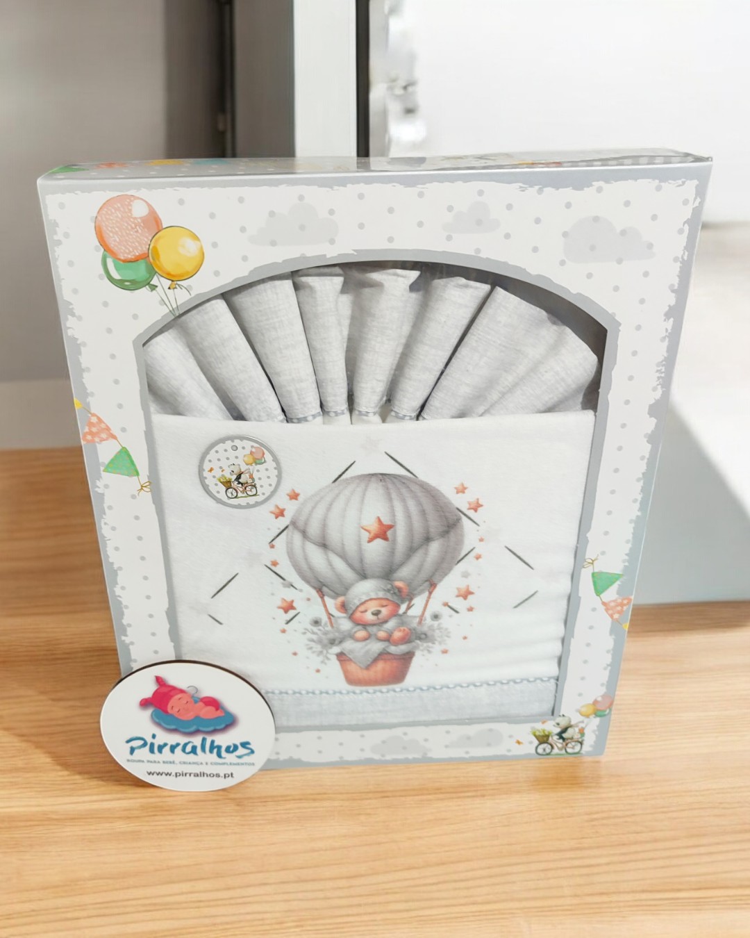 Conjunto de fraldas brancas com ilustração de urso em balão, embalagem com etiquetas da marca Pirralhos