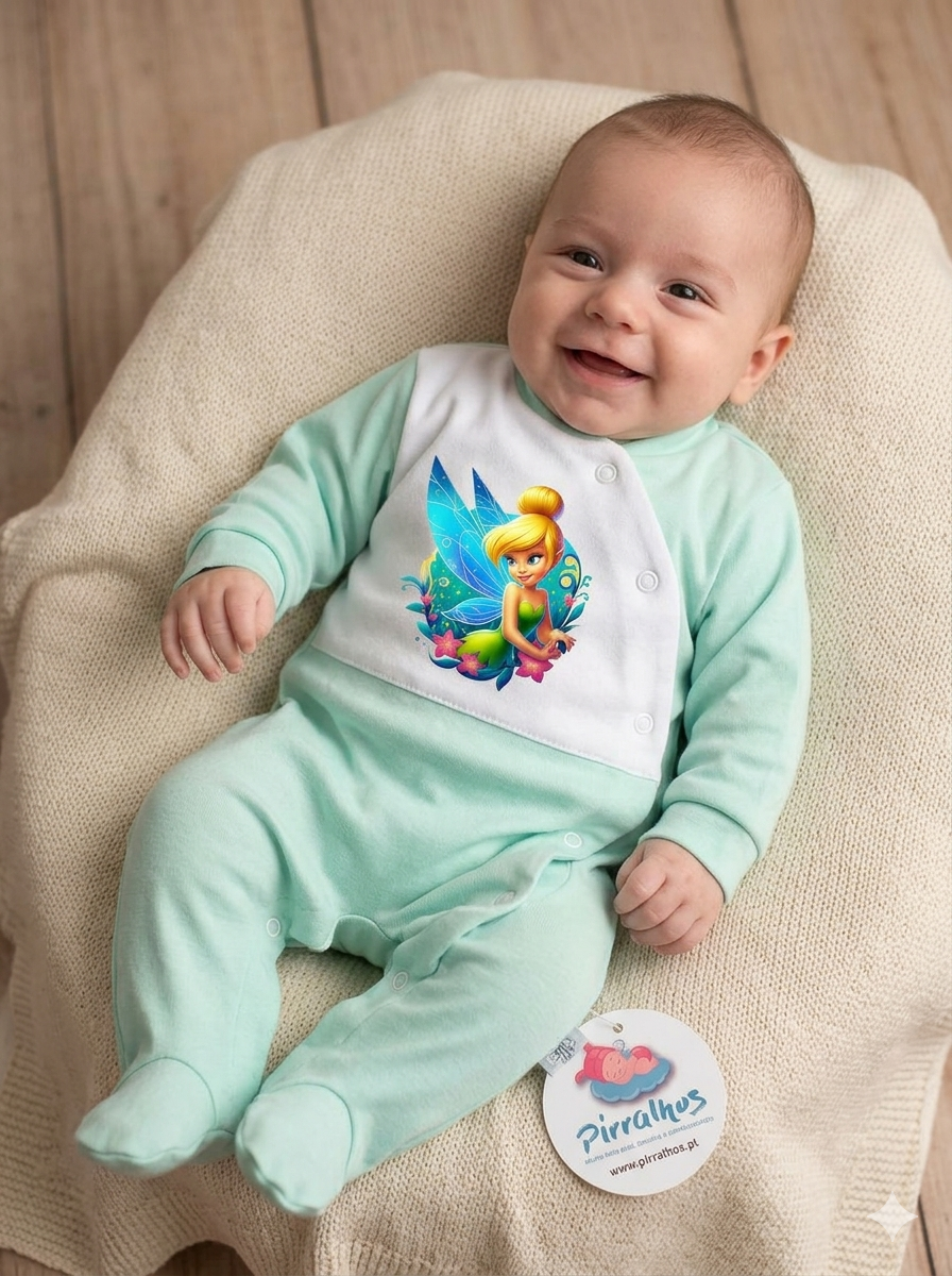 Bebé com pijama verde água e branco com imagem de fada sentado em tecido bege.