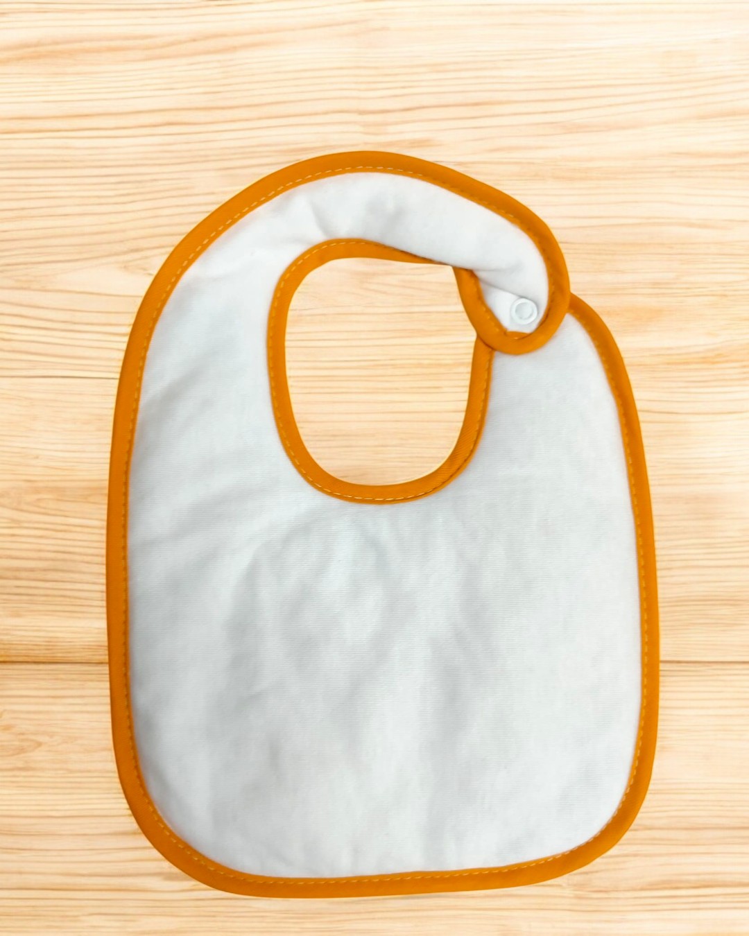 Babete infantil branco com bordas laranja e fecho de botão