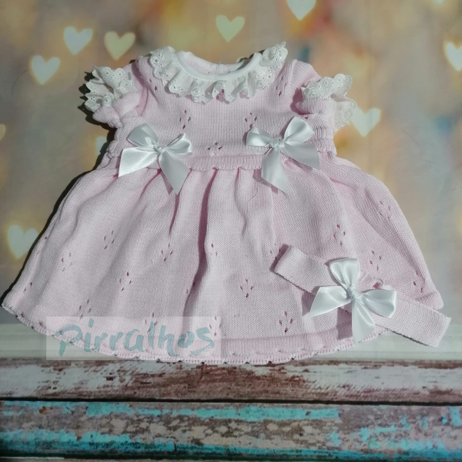 Vestido de bebé cor-de-rosa com laços brancos e renda, com fita combinando, fundo com corações desfocados