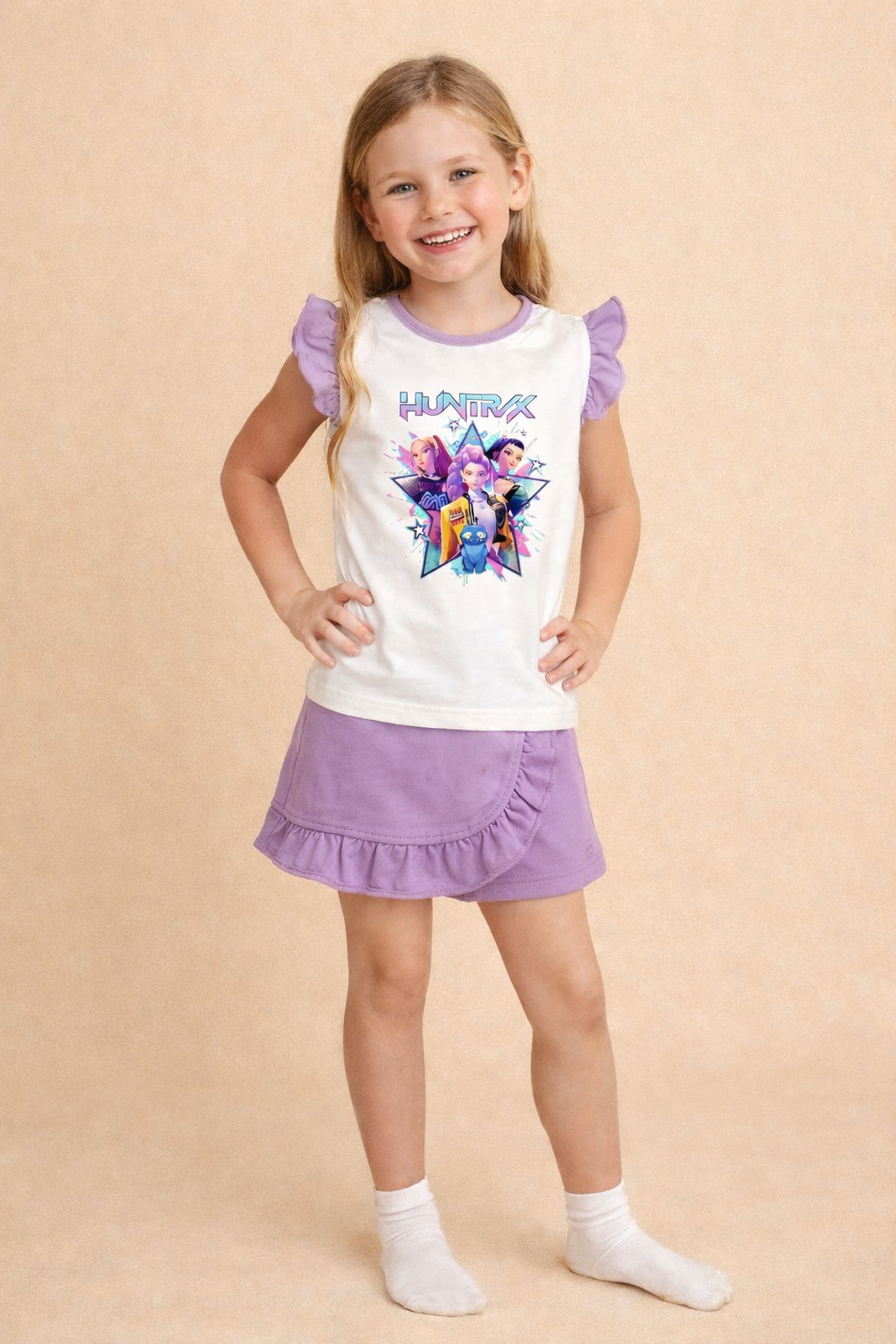 Menina com camisola branca e roxa com estampado HUNTRX e saia roxa com folhos numa pose sorridente.
