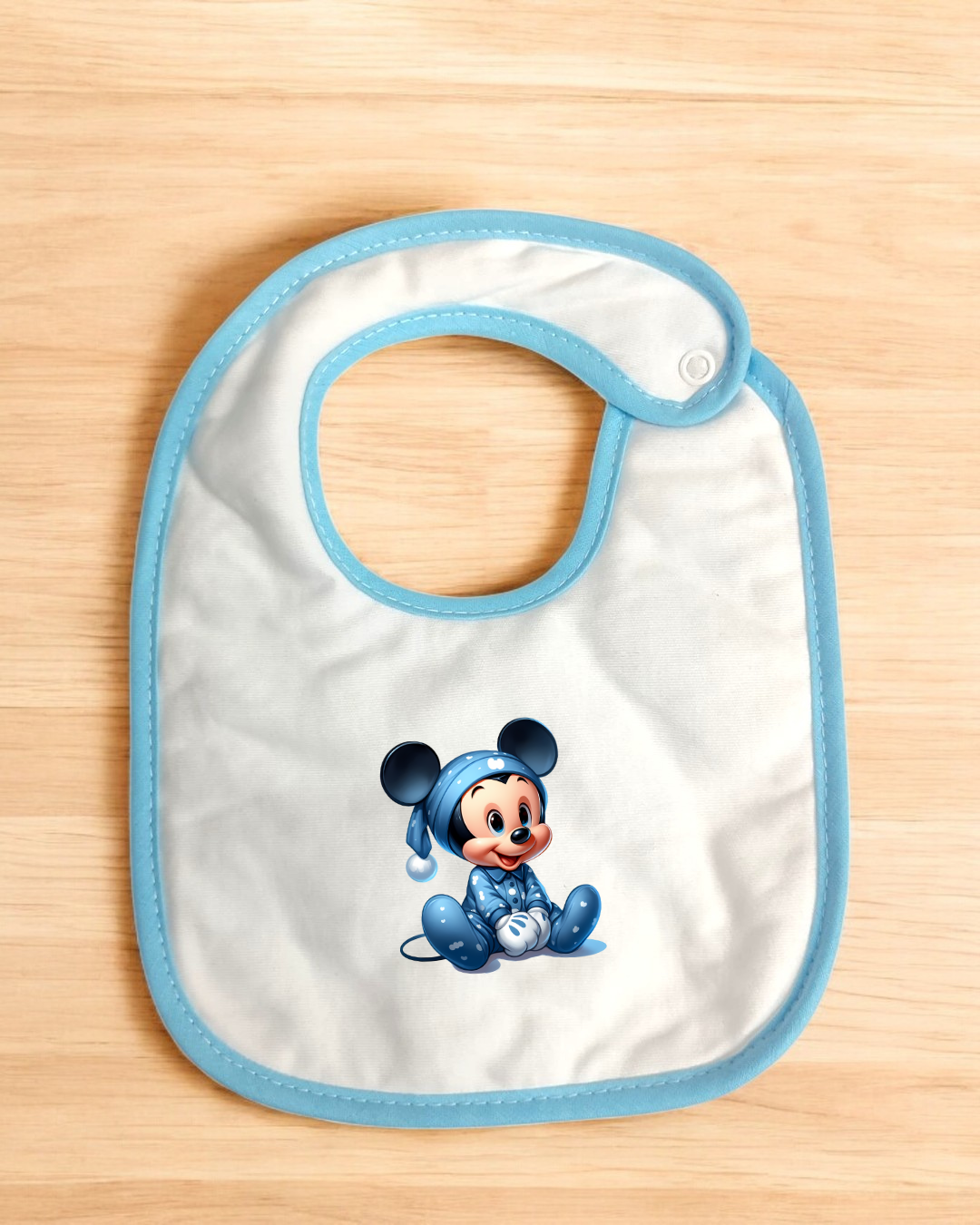 Babete branco com borda azul e imagem de Mickey Mouse em pijama azul