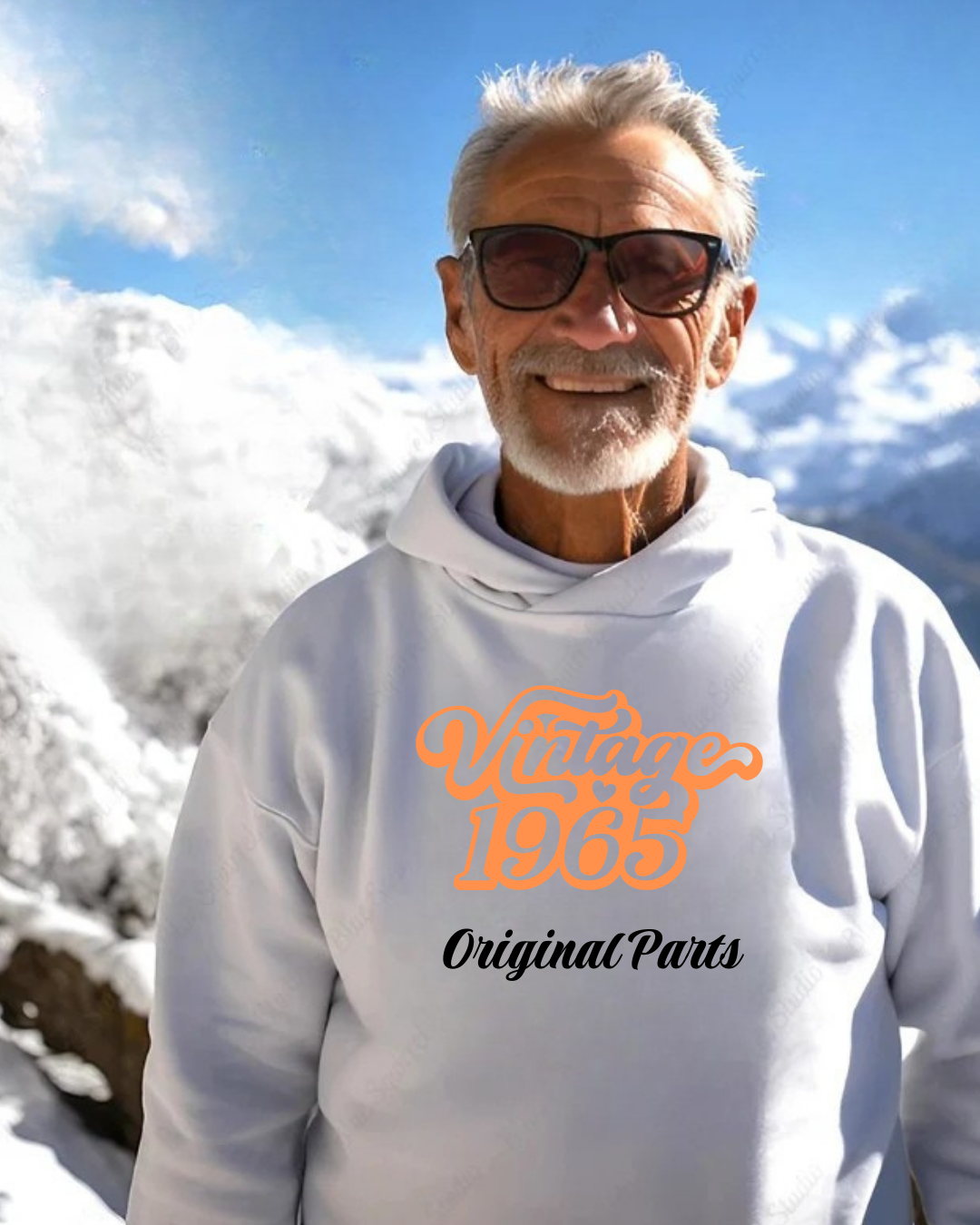 Homem idoso com sudadera branca com capuz e texto 'Vintage 1965 Original Parts' em montanhas nevadas.