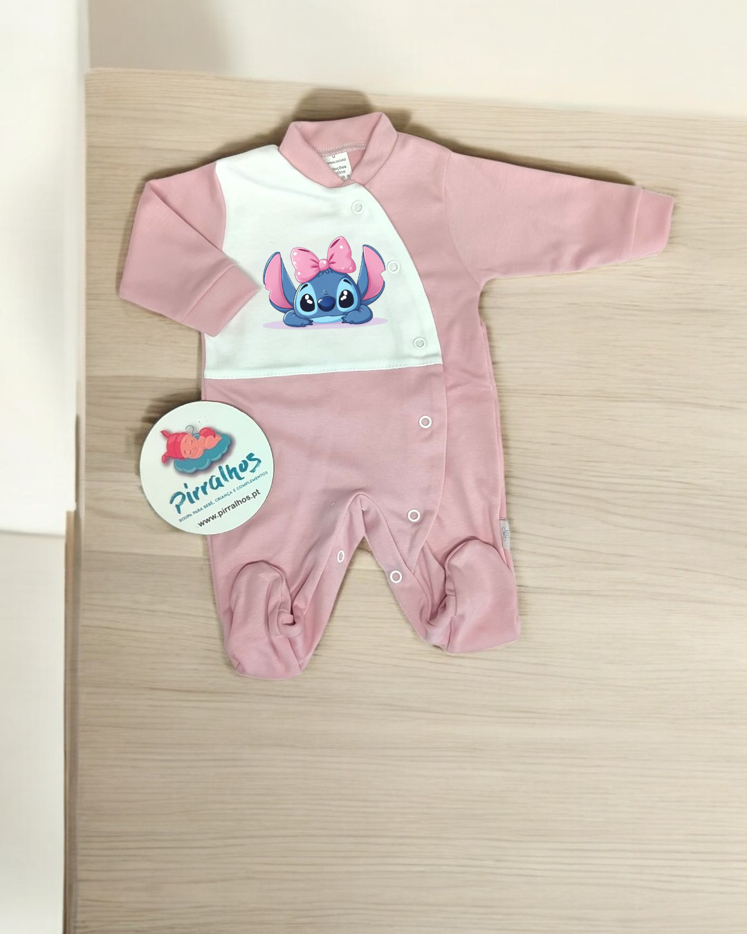 Macacão de bebé rosa e branco com estampado do personagem Stitch e etiqueta da marca Pirrilhos