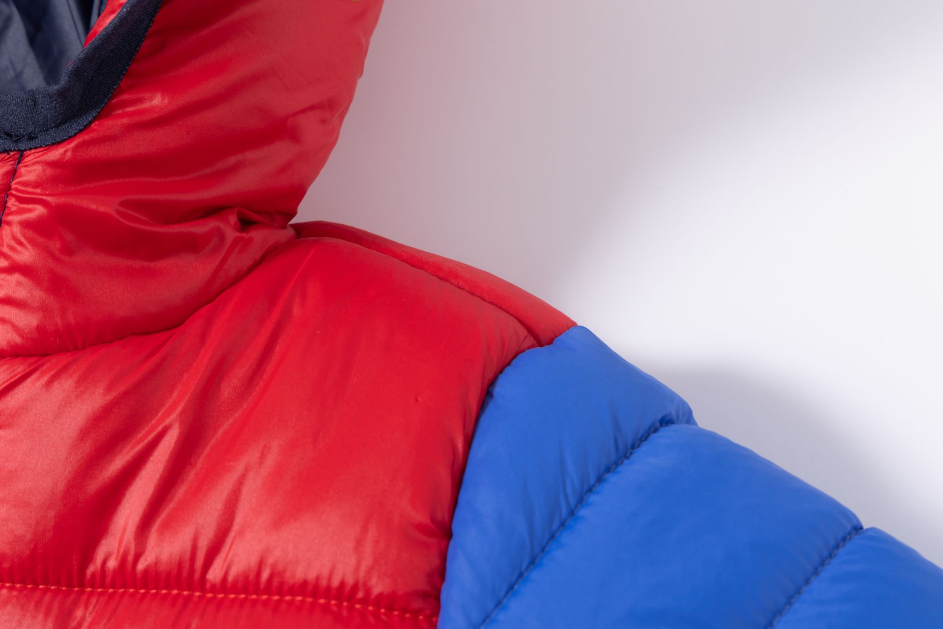 Casaco acolchoado vermelho e azul com capuz, em fundo branco