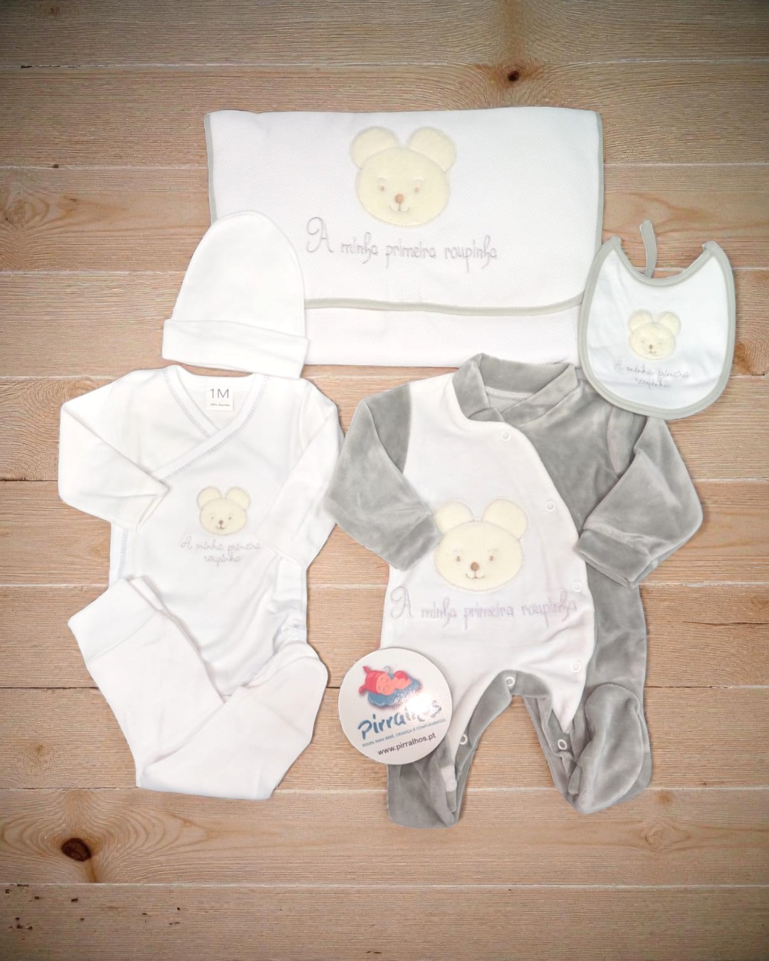 Conjunto de roupa para bebé branco e cinza com ursinho bordado sobre madeira clara