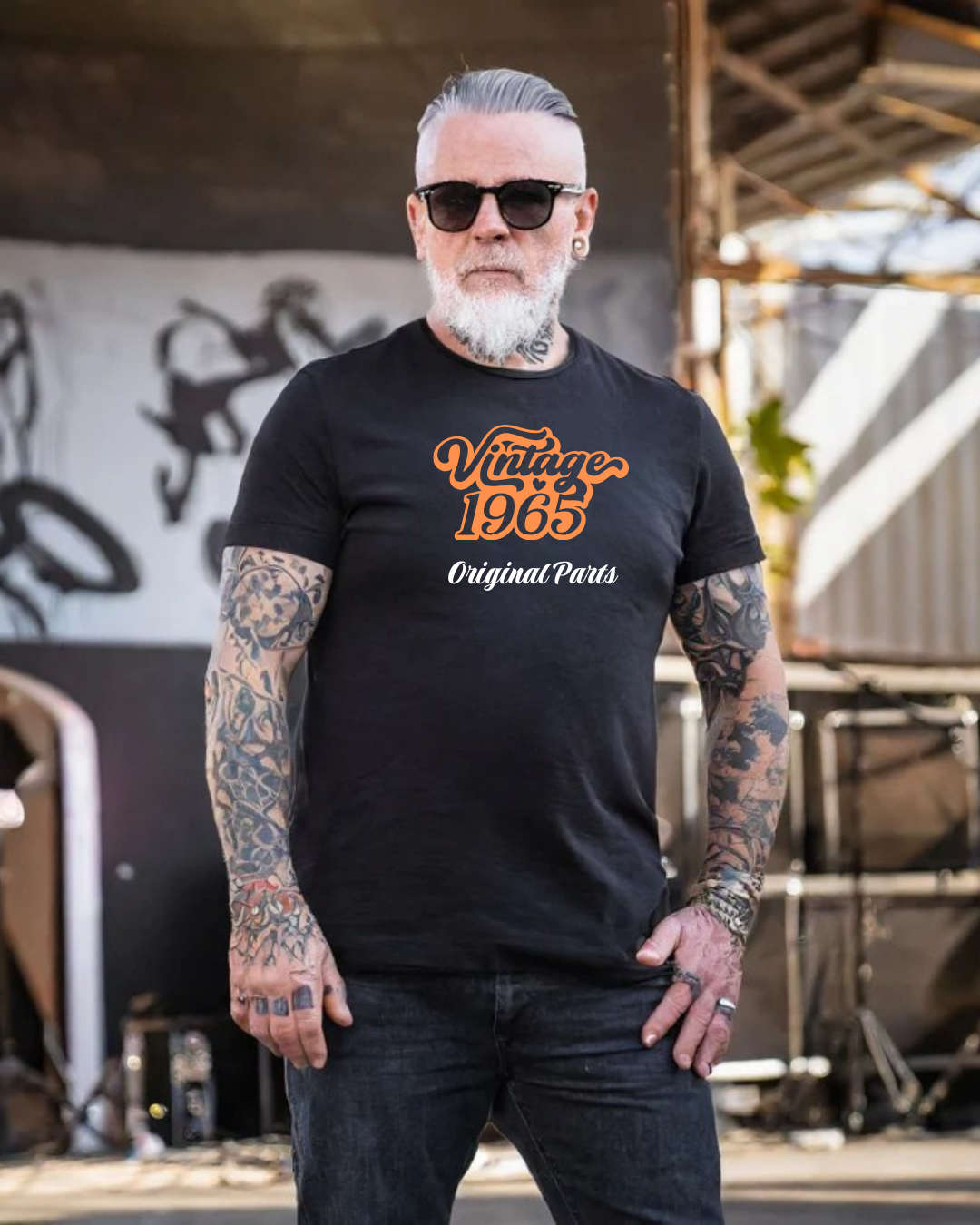 Homem com t-shirt preta e texto 'Vintage 1965 Original Parts' em ambiente industrial