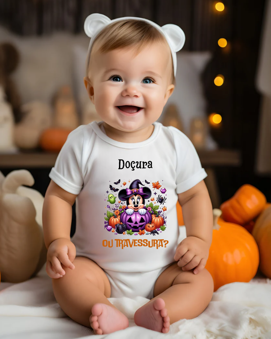 Bebé a vestir body branco com estampa colorida de Halloween e faixa branca com orelhas, sentado junto a abóboras.