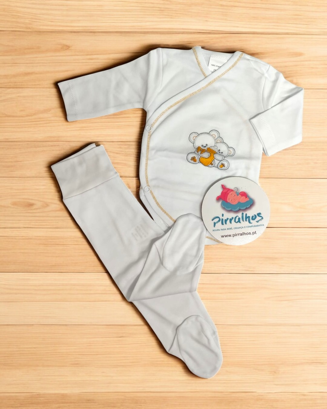 Conjunto de roupa de bebé branca com ursinho estampado e etiqueta da marca Pirralhos