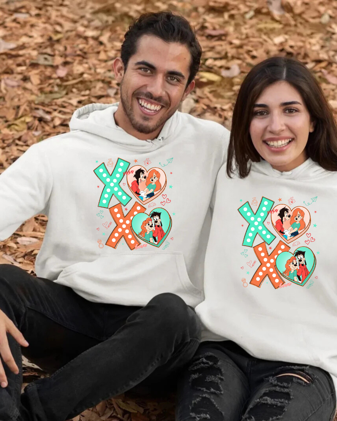 Dois jovens sentados ao ar livre com sweatshirts brancas com design colorido XOXO e ilustrações de casais