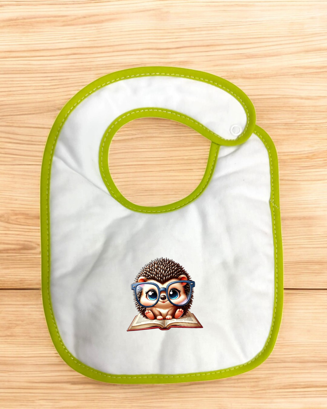 Babete branco com bordas verdes e desenho de ouriço de óculos sentado sobre livro.