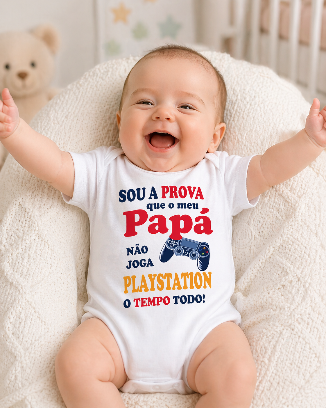 Body branco para bebé com texto colorido e comando de videojogo, bebé sorridente sentado num sofá claro.