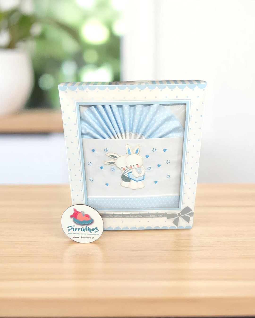 Caixa com toalha azul com coelho bordado e selo Pirralhos em mesa de madeira