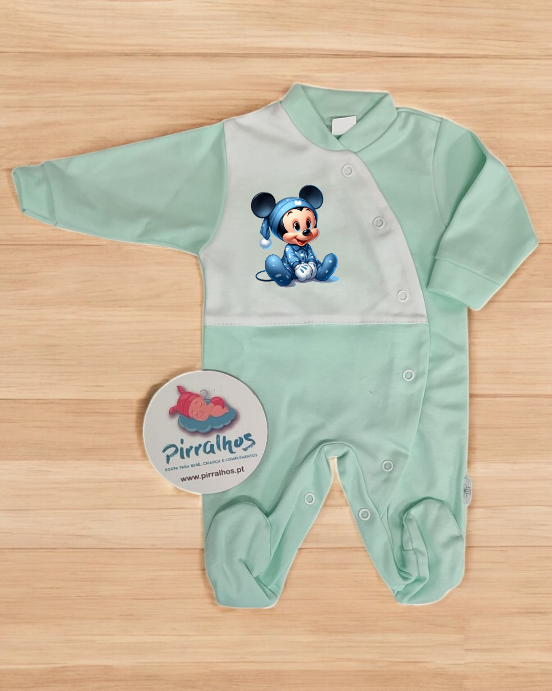Pijama de bebé verde e branco com imagem do Mickey bebés e botões de pressão em fundo de madeira