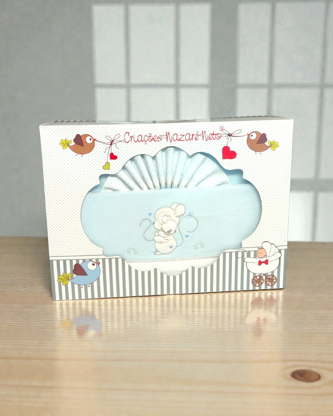 Conjunto de roupa de bebé azul claro com bordado de rato numa caixa decorada.
