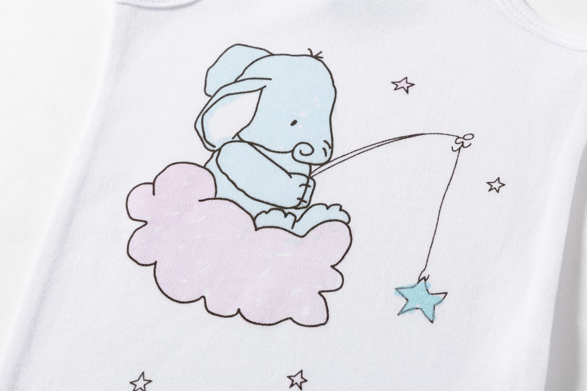 Peça de roupa branca com elefante azul numa nuvem rosa e estrela azul.