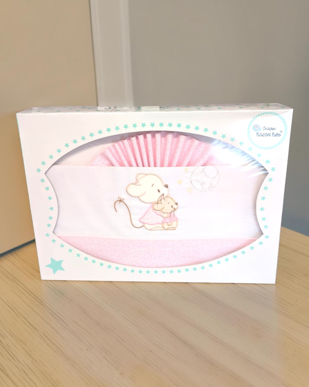 Conjunto de roupa de bebé rosa com bordado de ratinhos numa caixa com estrelas azuis.