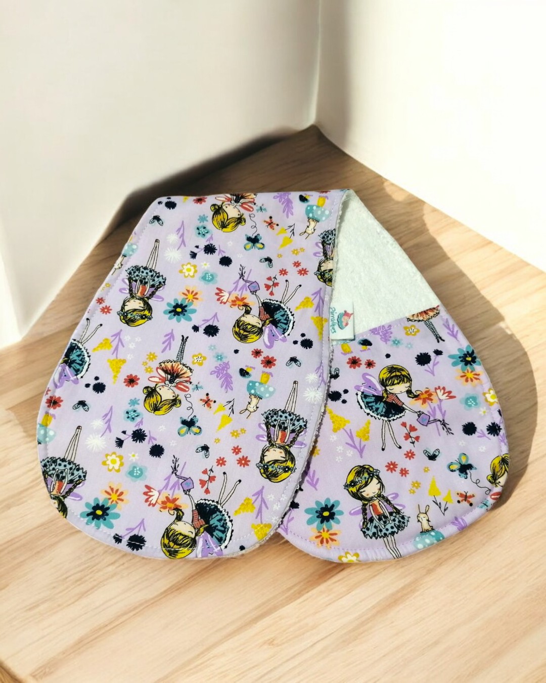 Dois panos de cozinha com padrão de bonecas e flores sobre mesa de madeira clara