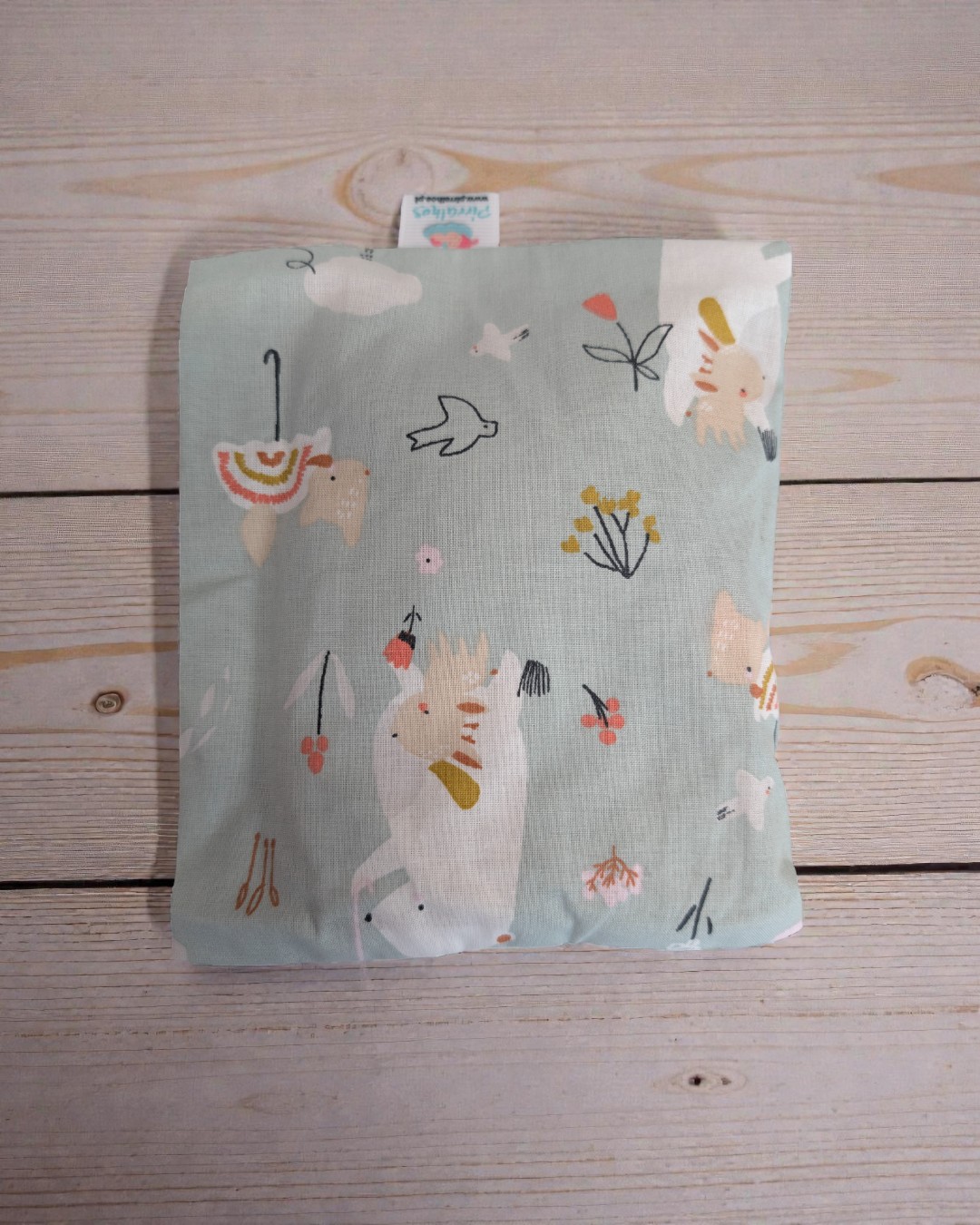 Almofada com padrão de animais e flores sobre superfície de madeira clara