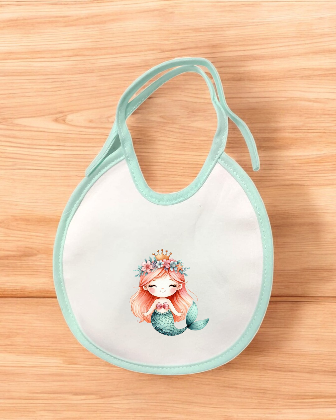 Babete branco com bordas azul claro e ilustração de sereia, sobre madeira clara