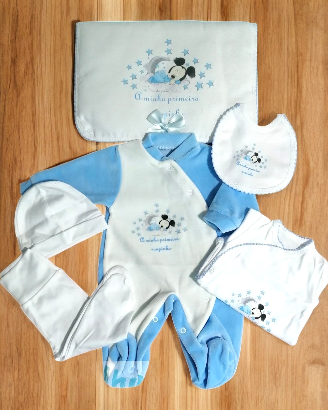 Conjunto de roupa de bebé azul e branca com bordados de ursinho e texto em português