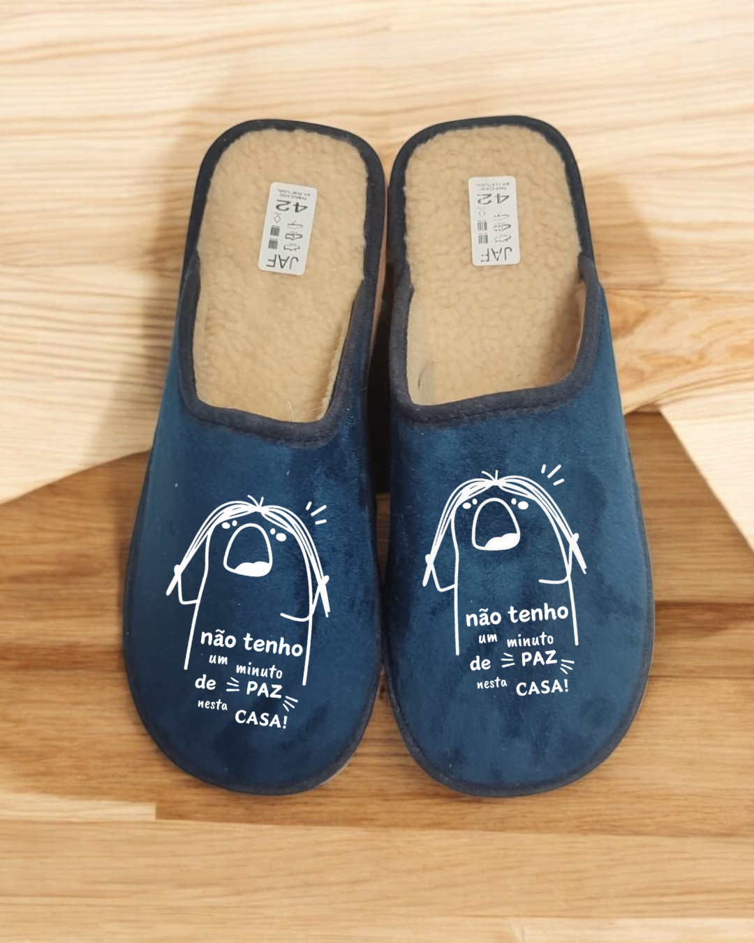 Chinelos azuis com interior felpudo bege e frase estampada em branco sobre chão de madeira claro
