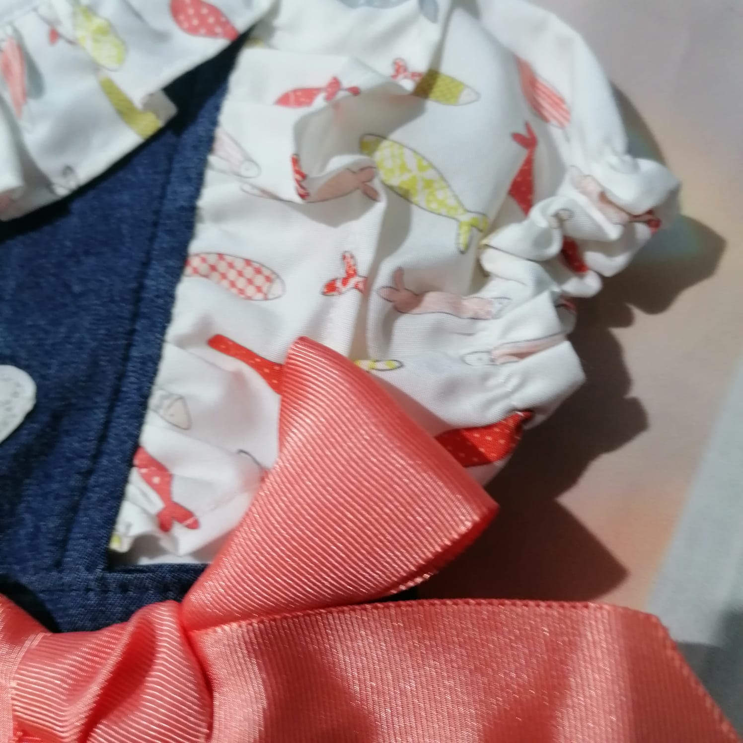 roupa branca com padrão de peixes coloridos, tecido franzido com elástico e laço cor de rosa