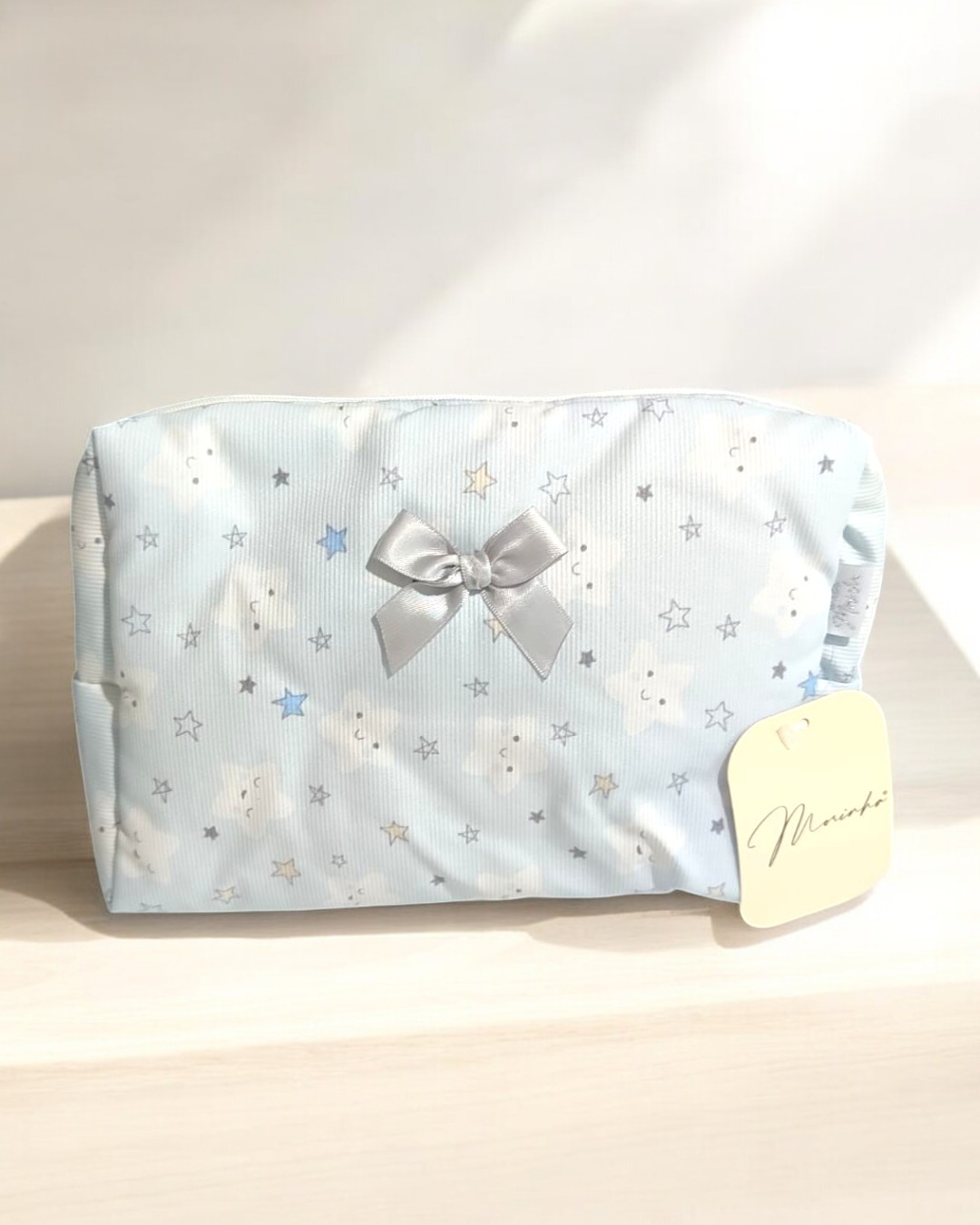 Necessaire azul claro com padrão de estrelas e nuvens, laço prateado e etiqueta 'Miranda'