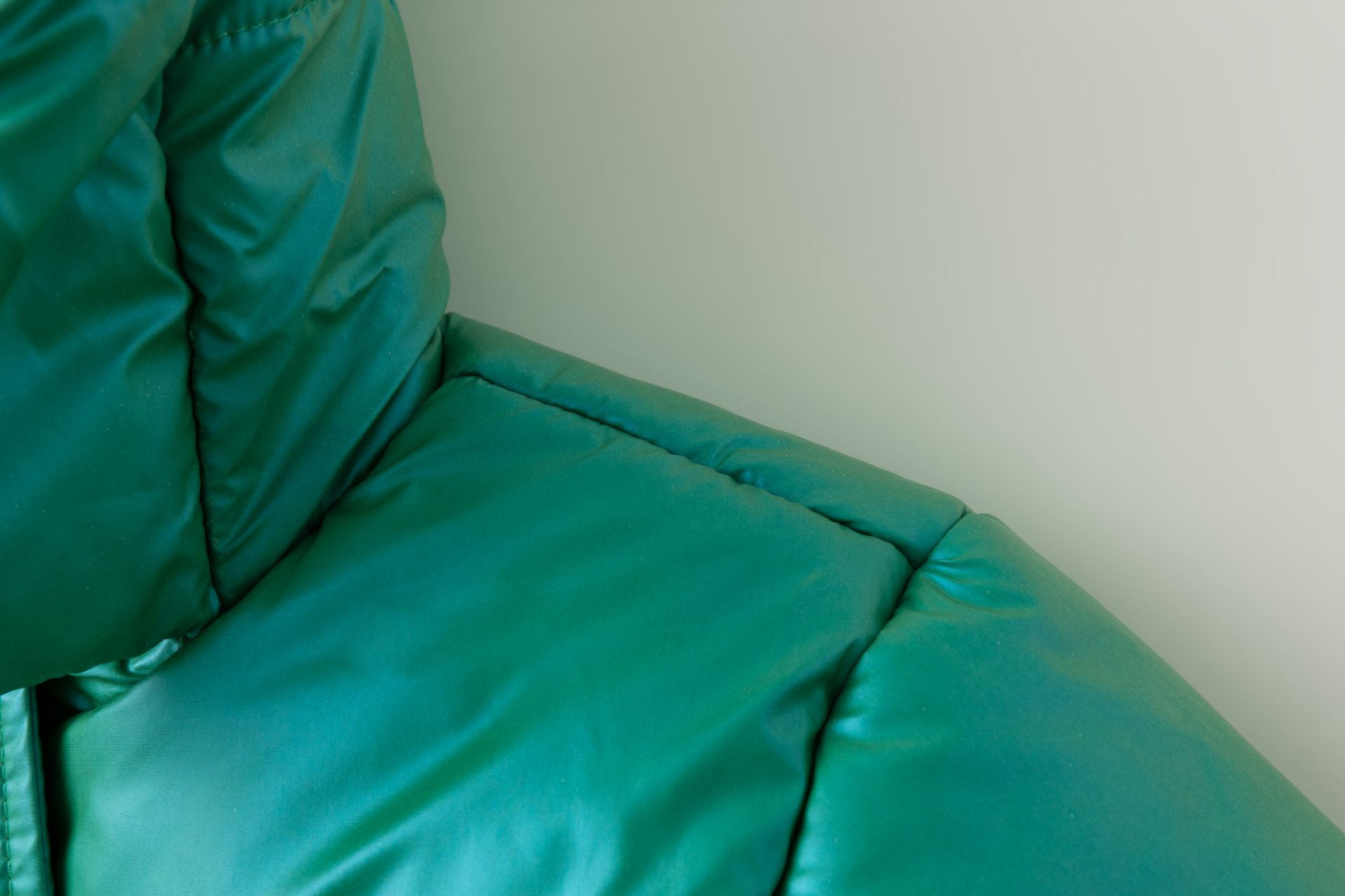 Sofá verde em couro com almofadas acolchoadas junto a uma parede branca