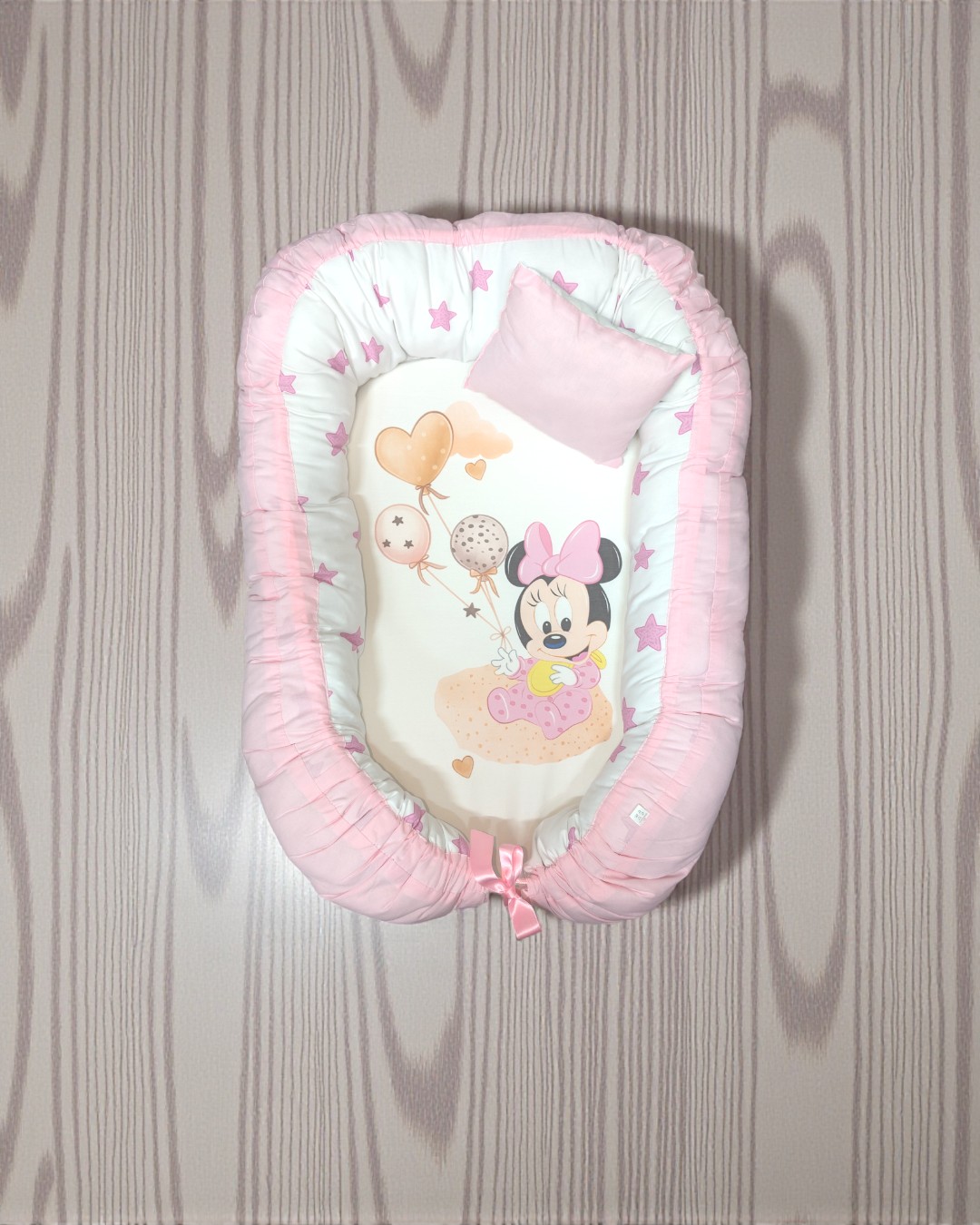 Ninho para bebé branco e rosa com ilustração da Minnie Mouse e balões, sobre chão de madeira clara.