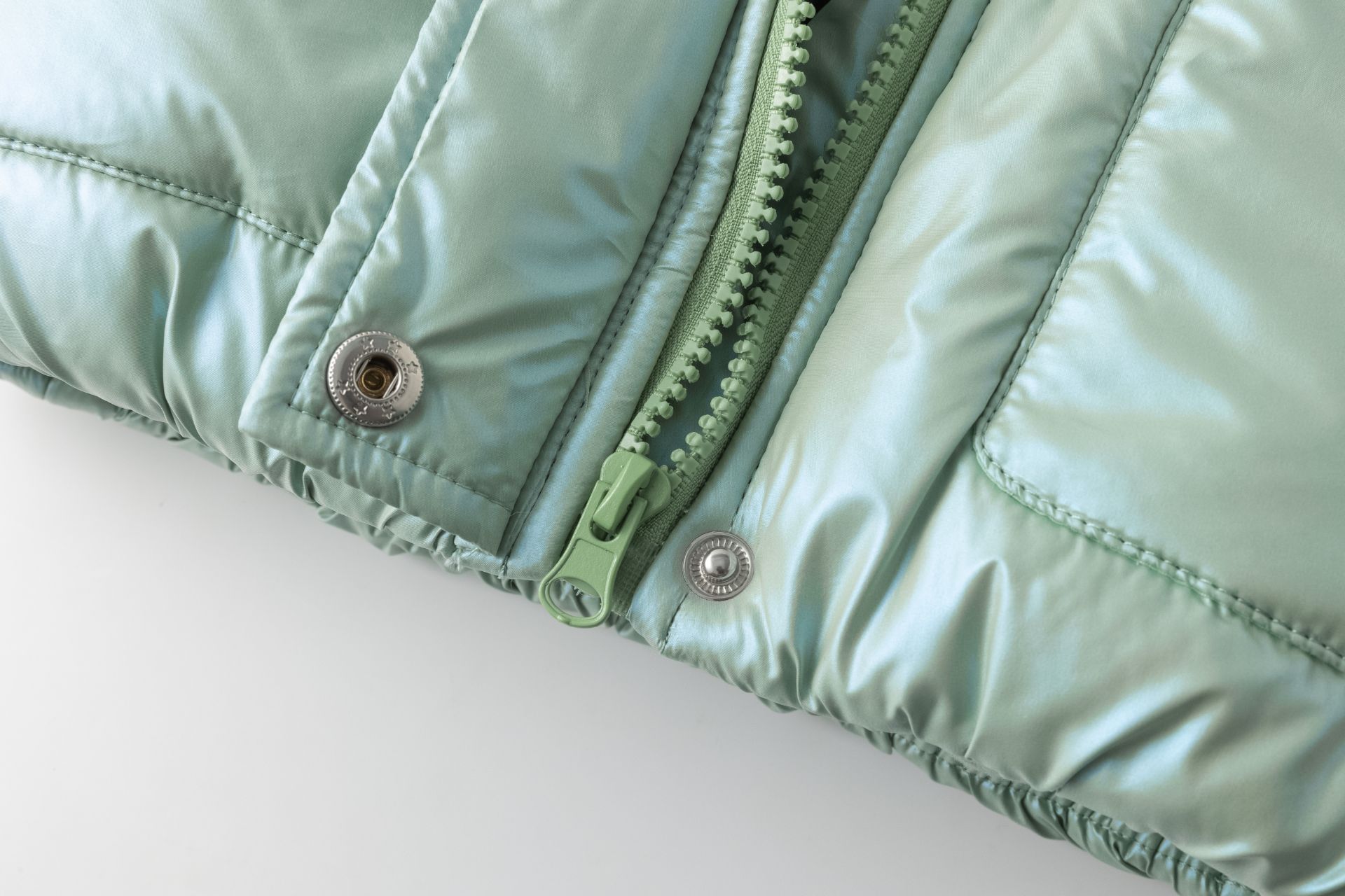 Detalhe inferior de casaco acolchoado verde claro com fecho de correr e molas metálicas