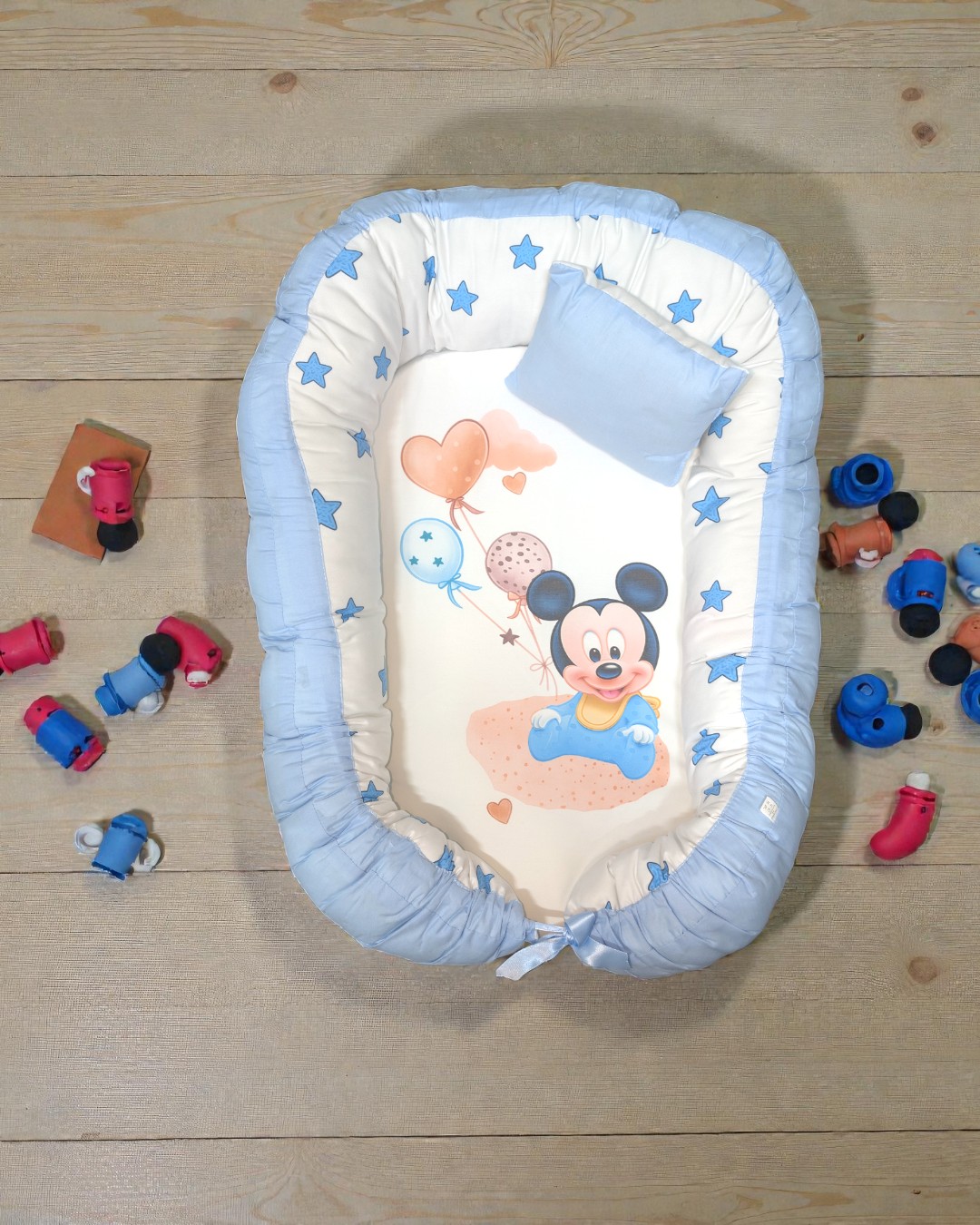 Ninho para bebé azul e branco com estampa do Mickey Mouse e almofada azul num chão de madeira com brinquedos.