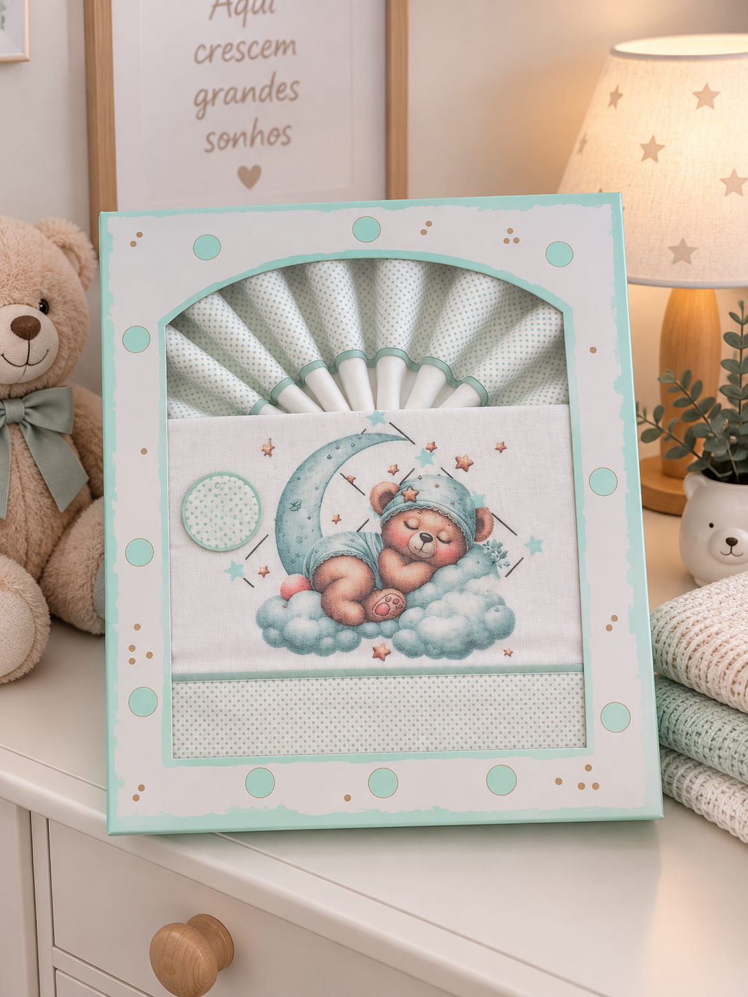 Conjunto de roupa de bebé com ursinho a dormir, em embalagem decorada com pontos verdes e dourados