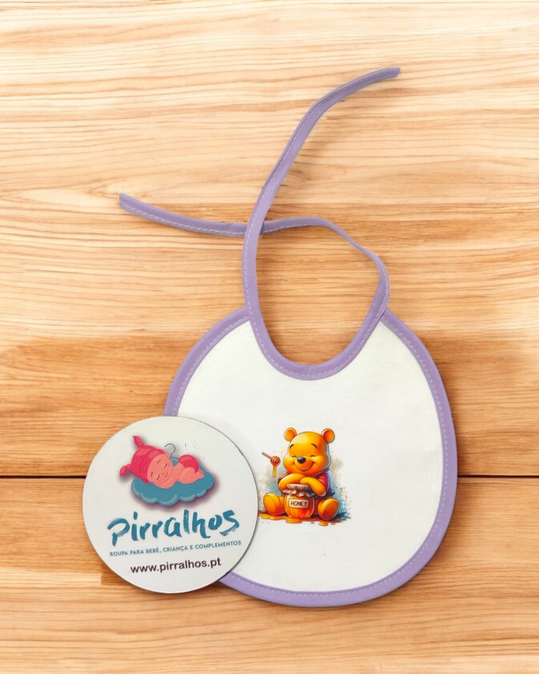 Babete branco com contorno roxo e estampa do Ursinho Pooh segurando pote de mel, com chapa redonda da marca Pirralhos.
