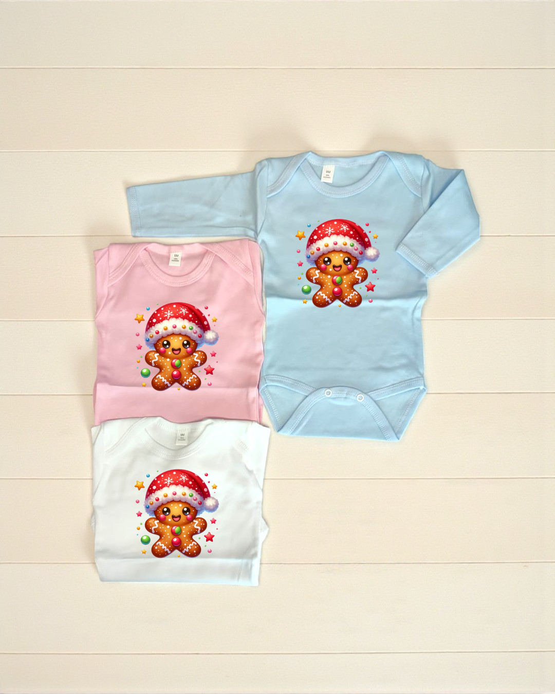 Três bodies para bebé com estampa de biscoito de gengibre natalício em azul claro, rosa e branco.