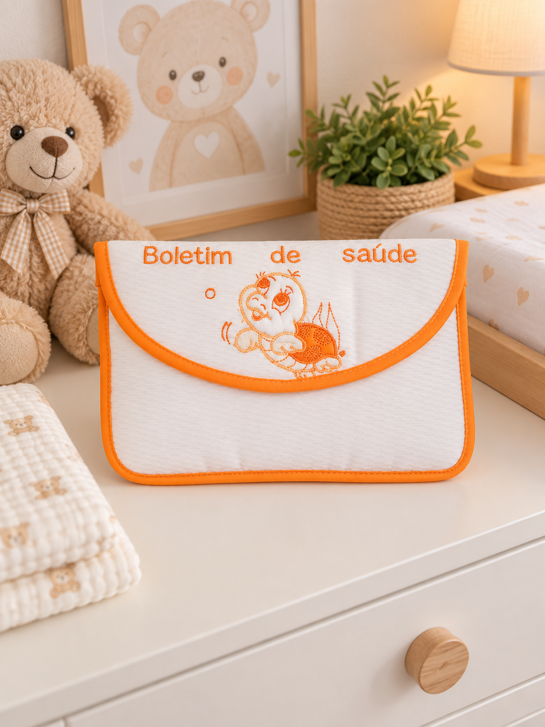 Capa branca com bordas e bordado laranja para boletim de saúde, em ambiente de quarto infantil.