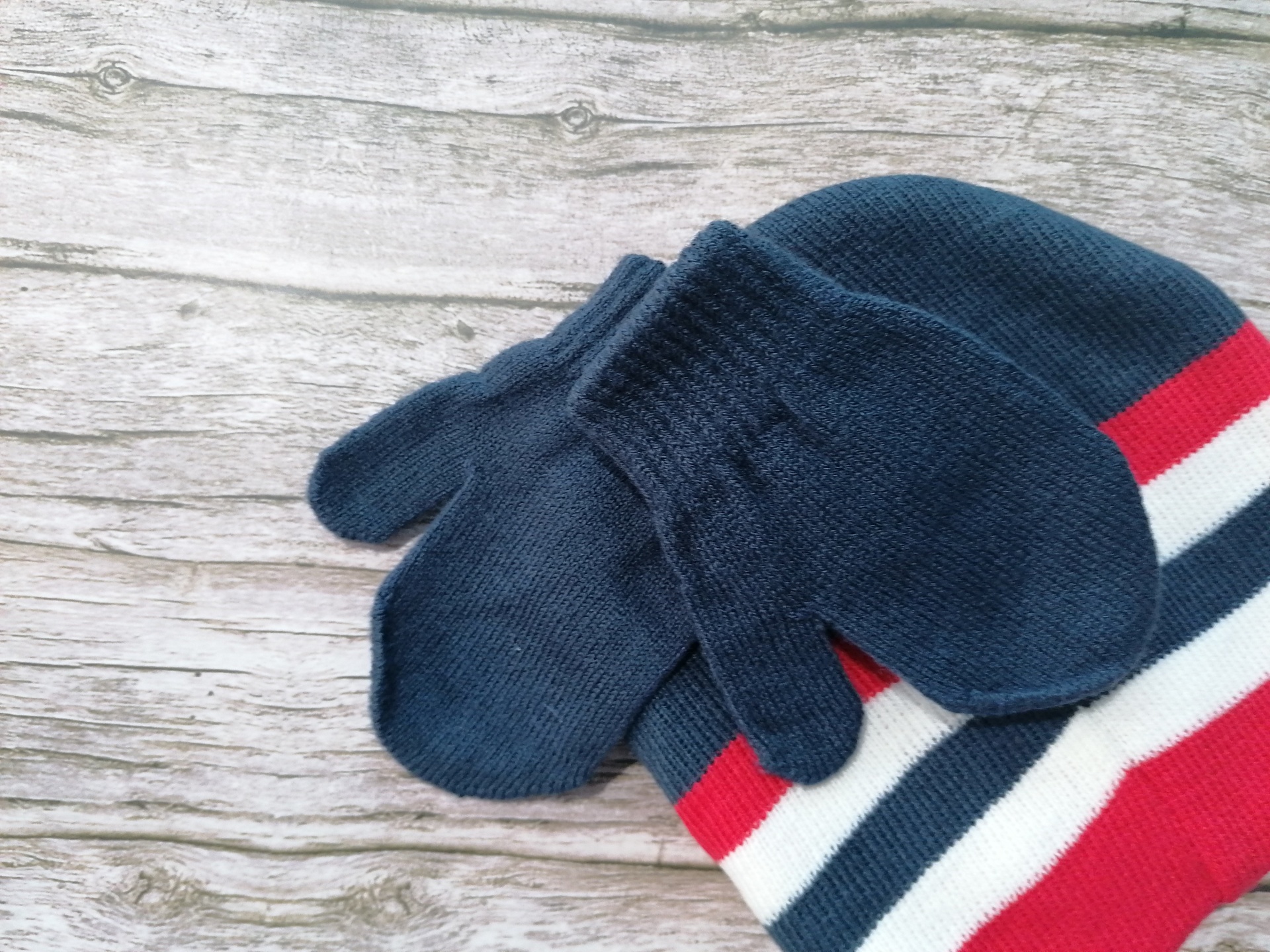 Luvas e gorro de malha azul escuro sobre tecido às riscas e madeira cinzenta