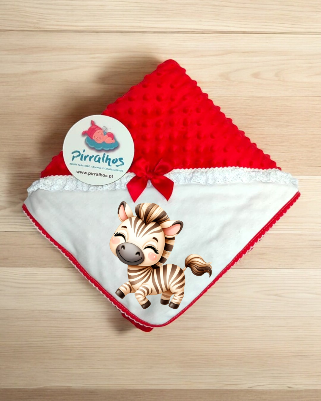 Manta de bebé vermelha e branca com etiqueta de marca Pirralhos sobre madeira clara