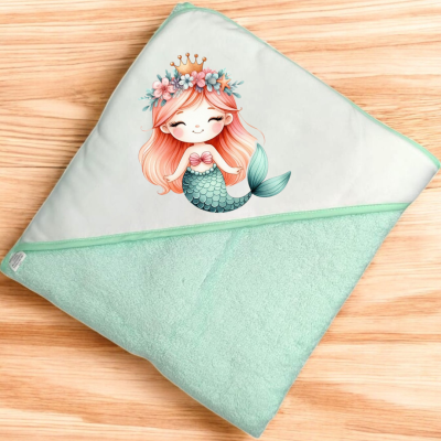 Toalha de bebé verde claro com imagem de sereia e coroa sobre superfície de madeira.
